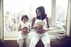 young child and mother sit in a window seat, comparing their bellies