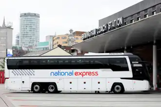 A white National Express coach parked in front of a smart, grey building: Birmingham Coach Station