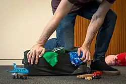 man tries to close an overstuffed suitcase of children's clothes and toys